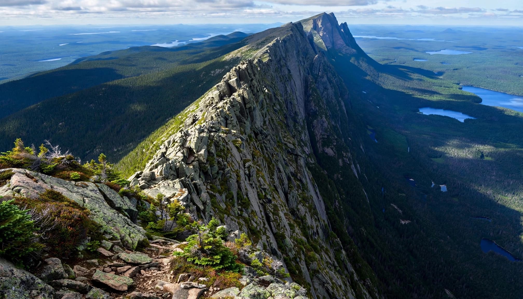 A jagged granite ridge rises above evergreen forest and distant lakes.