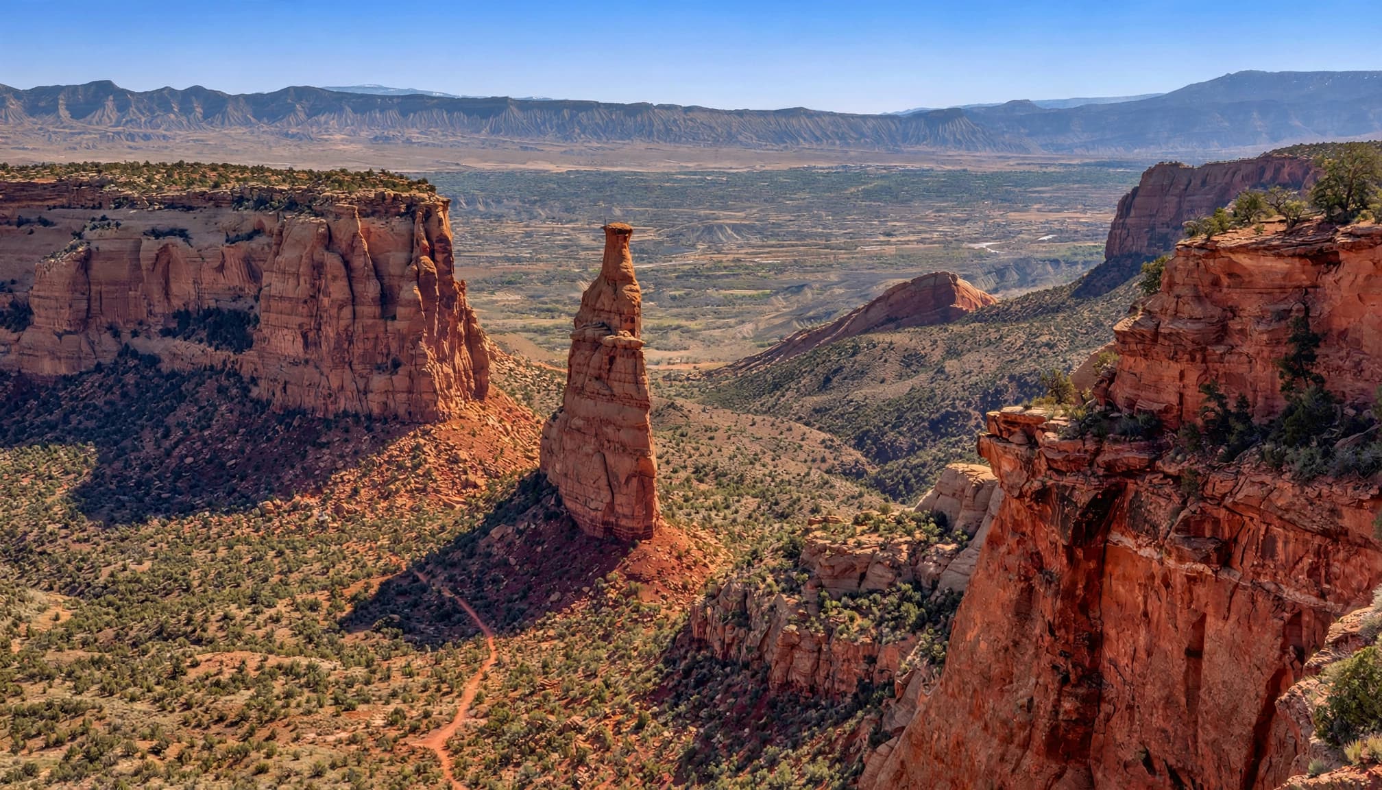 Independence Monument rises above red cliffs and a narrow trail on the canyon floor.