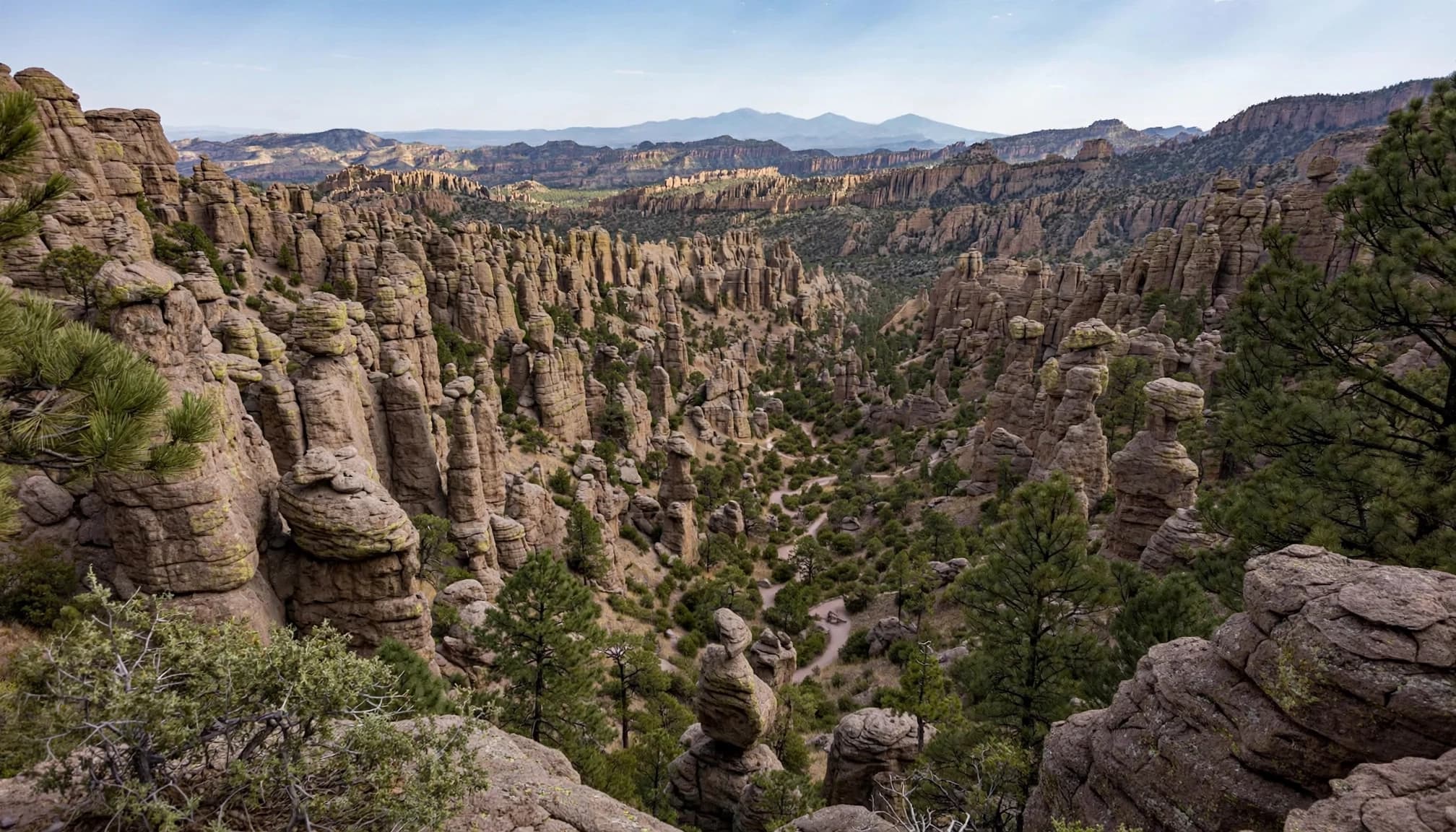 A sweeping landscape view of rocky hoodoos and spires in Chiricahua National Monument with a winding trail below.