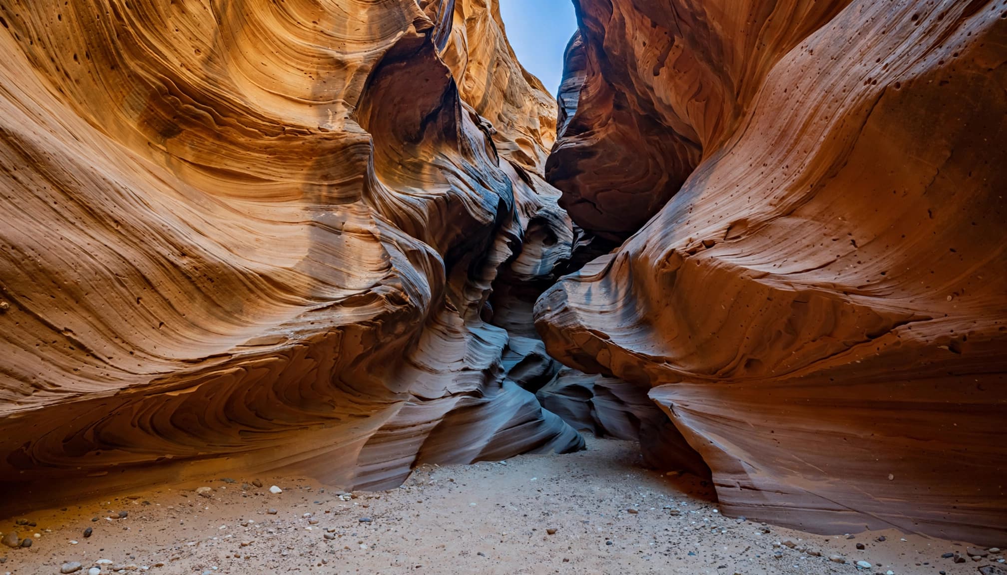 A narrow winding slot canyon with smooth sculpted sandstone walls and a strip of blue sky overhead.